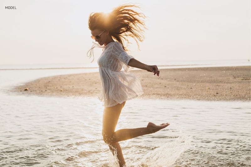 Woman jumping and splashing through the water on beach.
