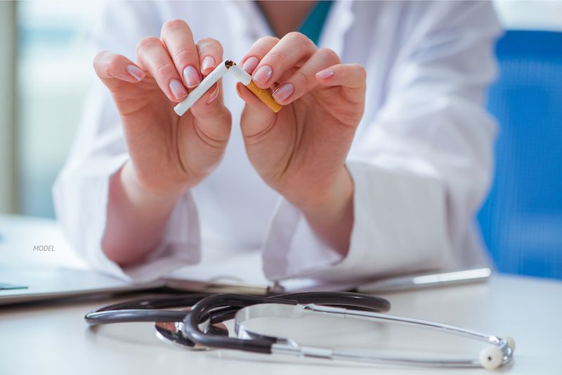 Doctor breaking a cigarette in half while seated at a desk
