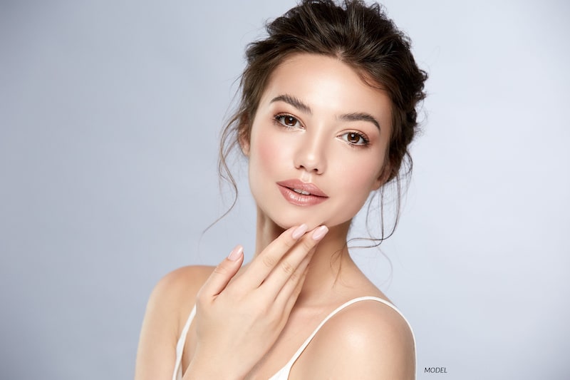 Young, beautiful woman touching her chin against a gray background
