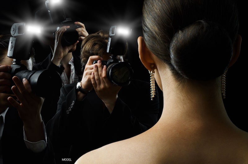 Photographers snap photos of a beautiful woman with her back turned to the camera.